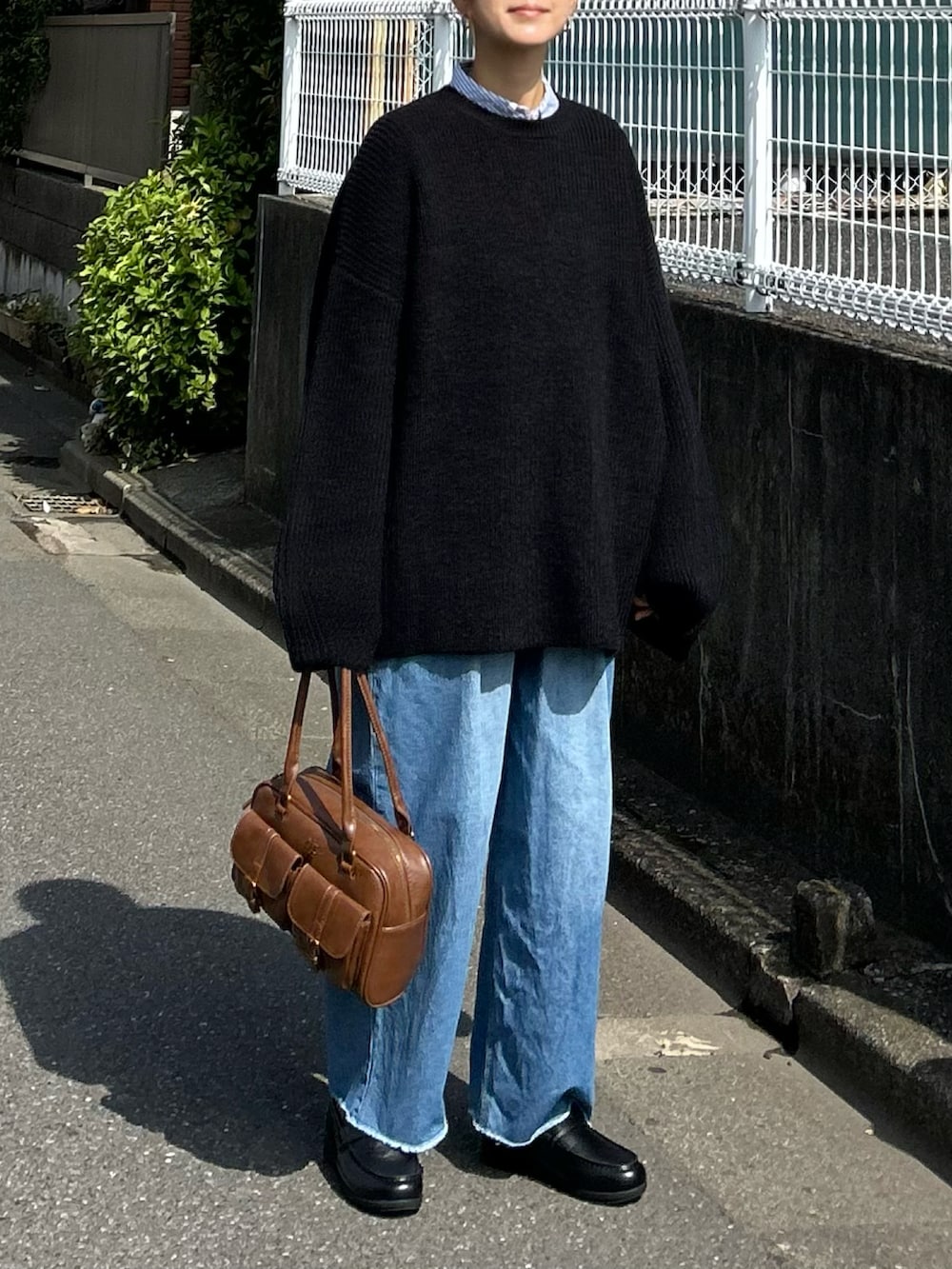 ブラック系のニット/セーター、ブルー系のデニムパンツ、ブラウン系のハンドバッグを着用したレディースの秋コーディネートの4枚目の写真