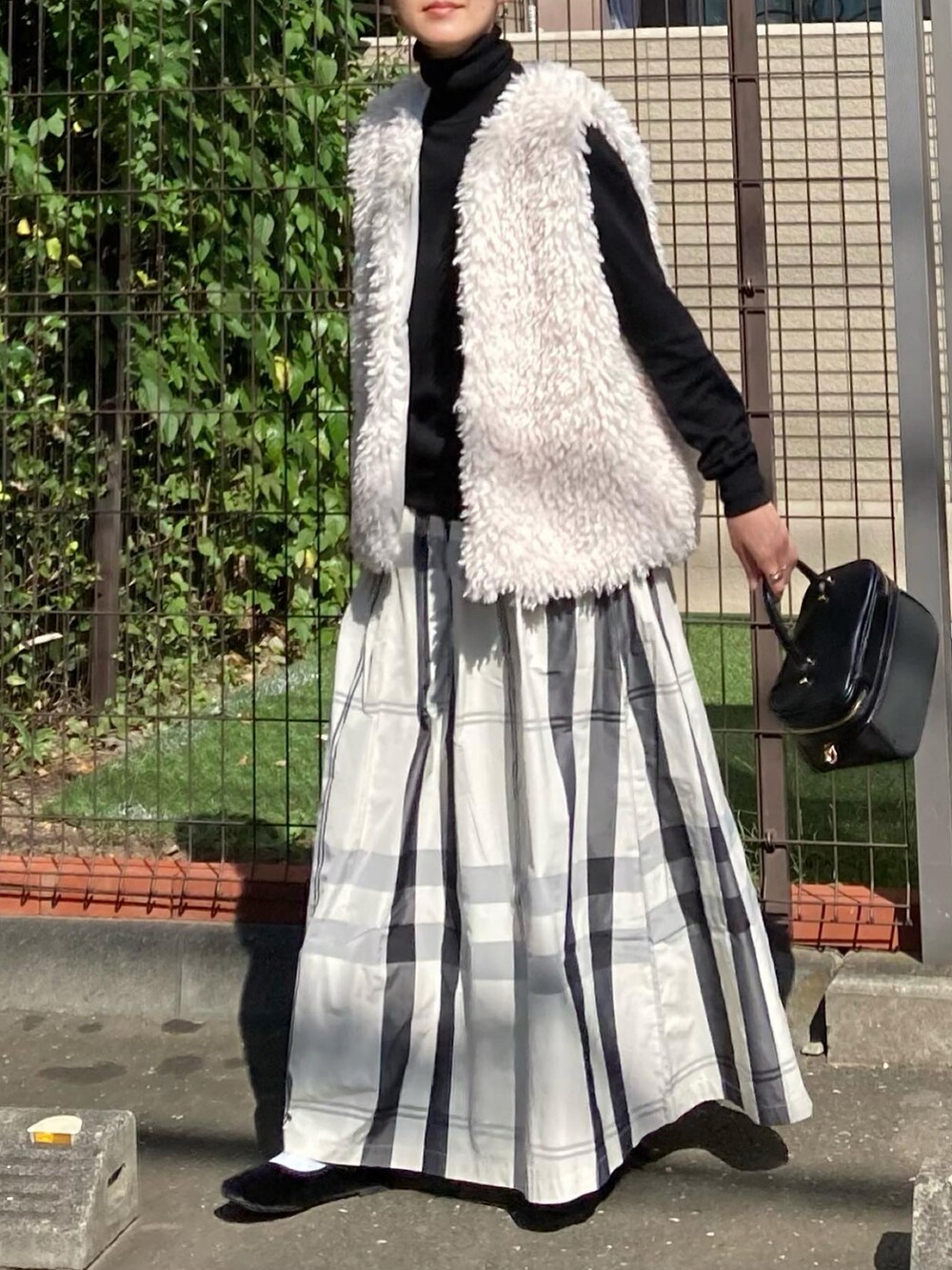 ホワイト系のベスト、ホワイト系のスカート、ブラック系のショルダーバッグを着用したレディースの秋コーディネートの2枚目の写真