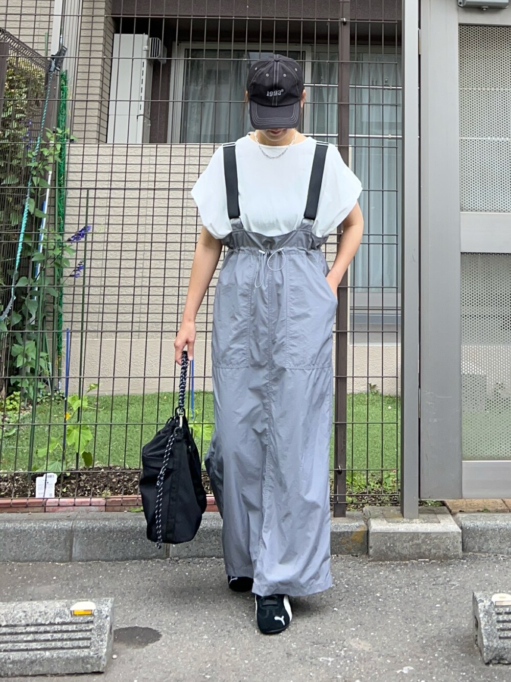 グレー系のジャンパースカート、ブラック系のトートバッグ、ブラック系のスニーカーを着用したレディースの夏コーディネートの2枚目の写真