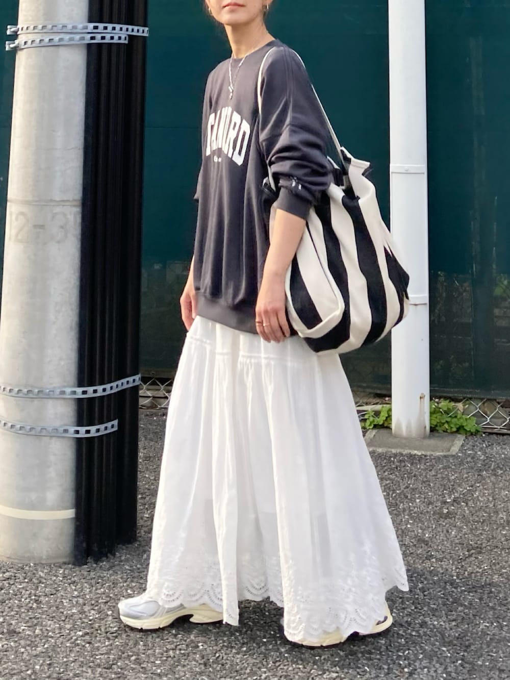 ブラック系のスウェット、ブラック系のトートバッグ、ホワイト系のスカートを着用したレディースの春コーディネートの2枚目の写真