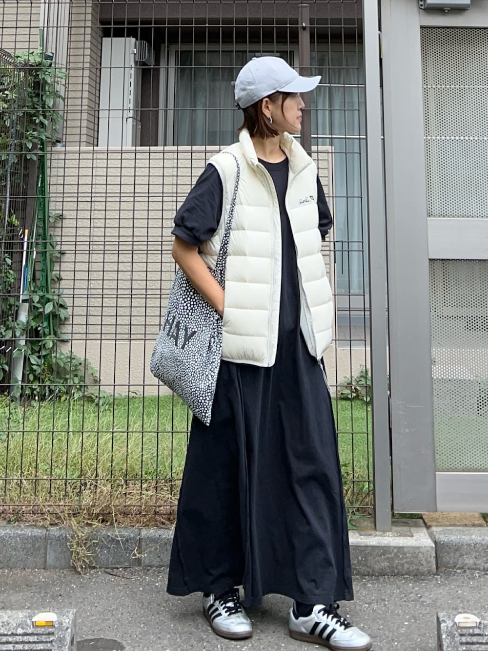 ホワイト系のダウンベスト、ブラック系のワンピース、ホワイト系のスニーカーを着用したレディースの秋コーディネートの2枚目の写真