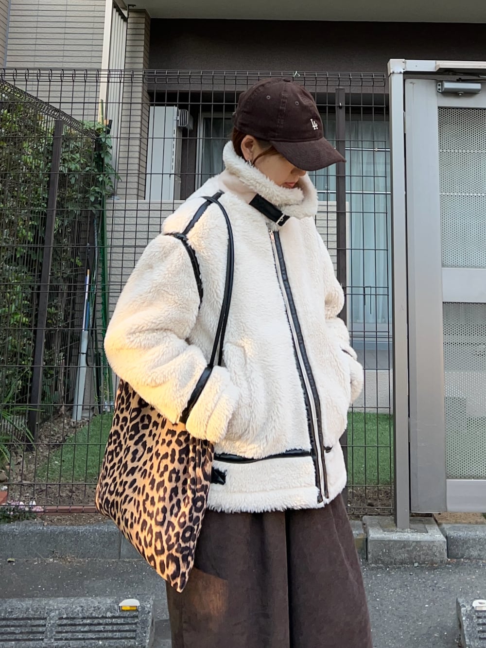 ホワイト系のムートンコート、ブラウン系のトートバッグ、ブラウン系のスラックスを着用したレディースの冬コーディネートの3枚目の写真