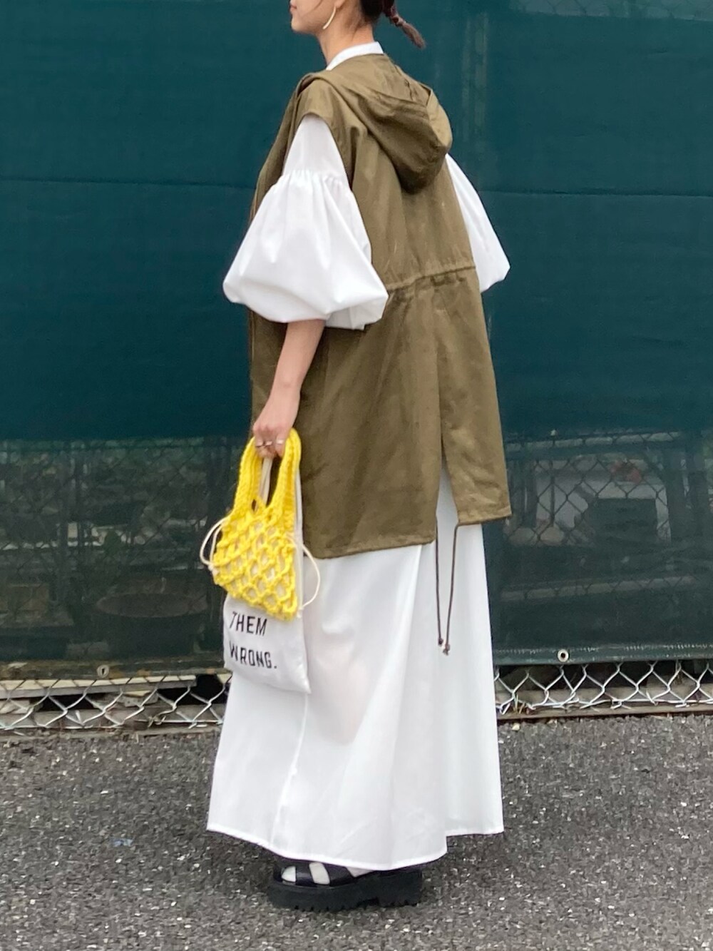 グリーン系のミリタリージャケット、ホワイト系のワンピース、イエロー系のハンドバッグを着用したレディースの春コーディネートの4枚目の写真