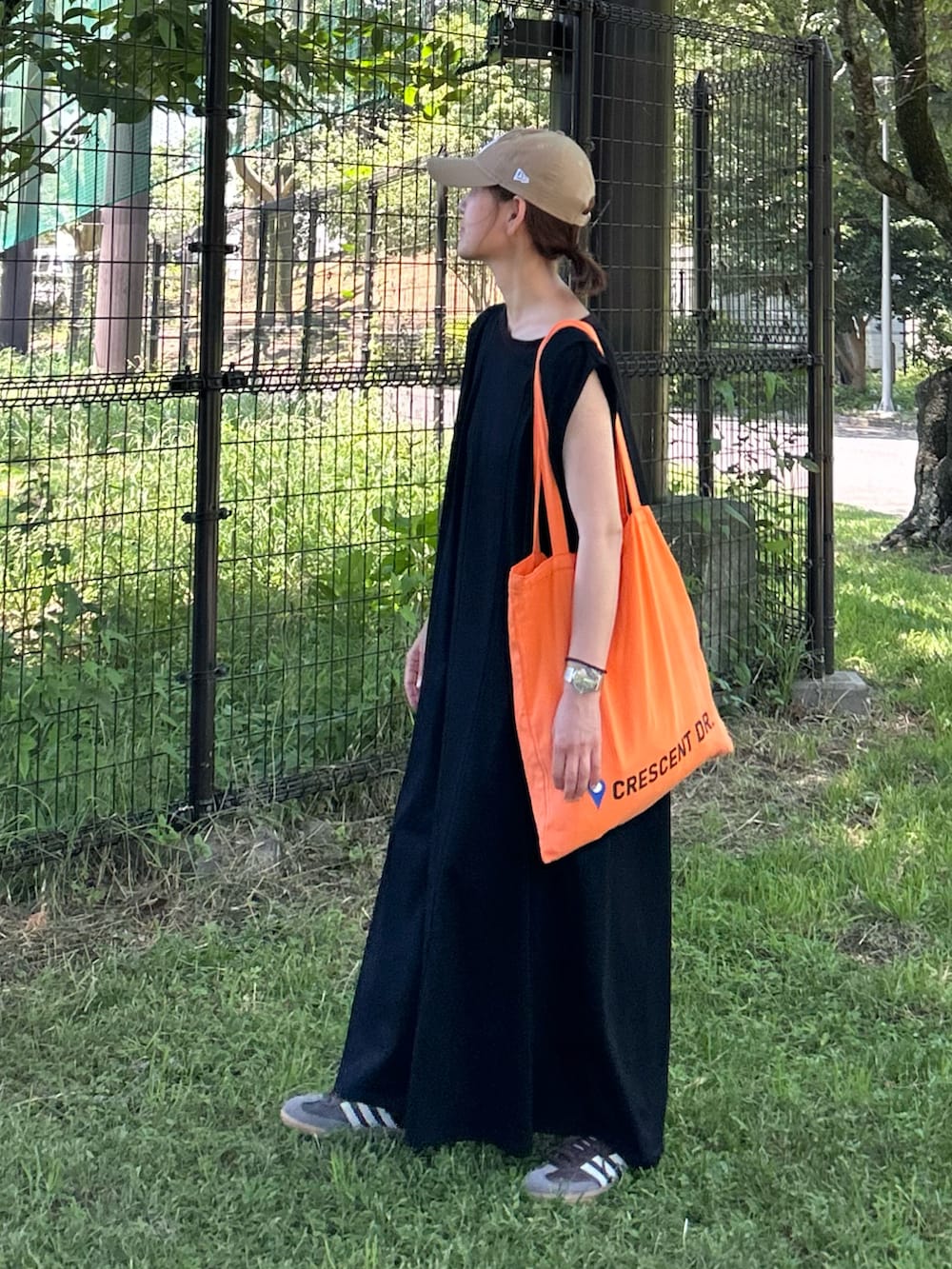 ブラック系のワンピース、オレンジ系のトートバッグ、ブラウン系のスニーカーを着用したレディースの夏コーディネートの2枚目の写真