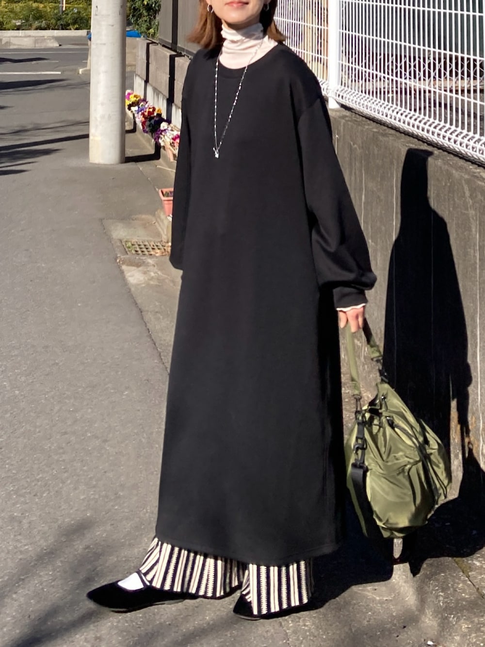 ブラック系のワンピース、ブラック系のその他パンツ、グリーン系のショルダーバッグを着用したレディースの冬コーディネートの2枚目の写真