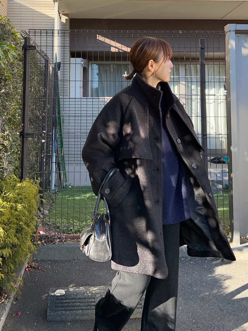 ブラック系のステンカラーコート、ブルー系のニット/セーター、ブラック系のその他パンツを着用したレディースの冬コーディネートの2枚目の写真