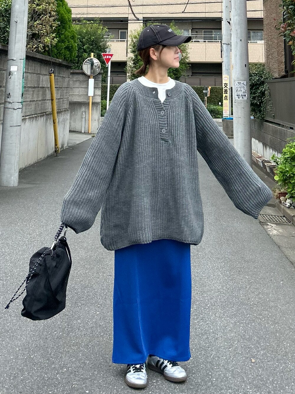 グレー系のニット/セーター、ブラック系のショルダーバッグ、ブルー系のスカートを着用したレディースの秋コーディネートの2枚目の写真