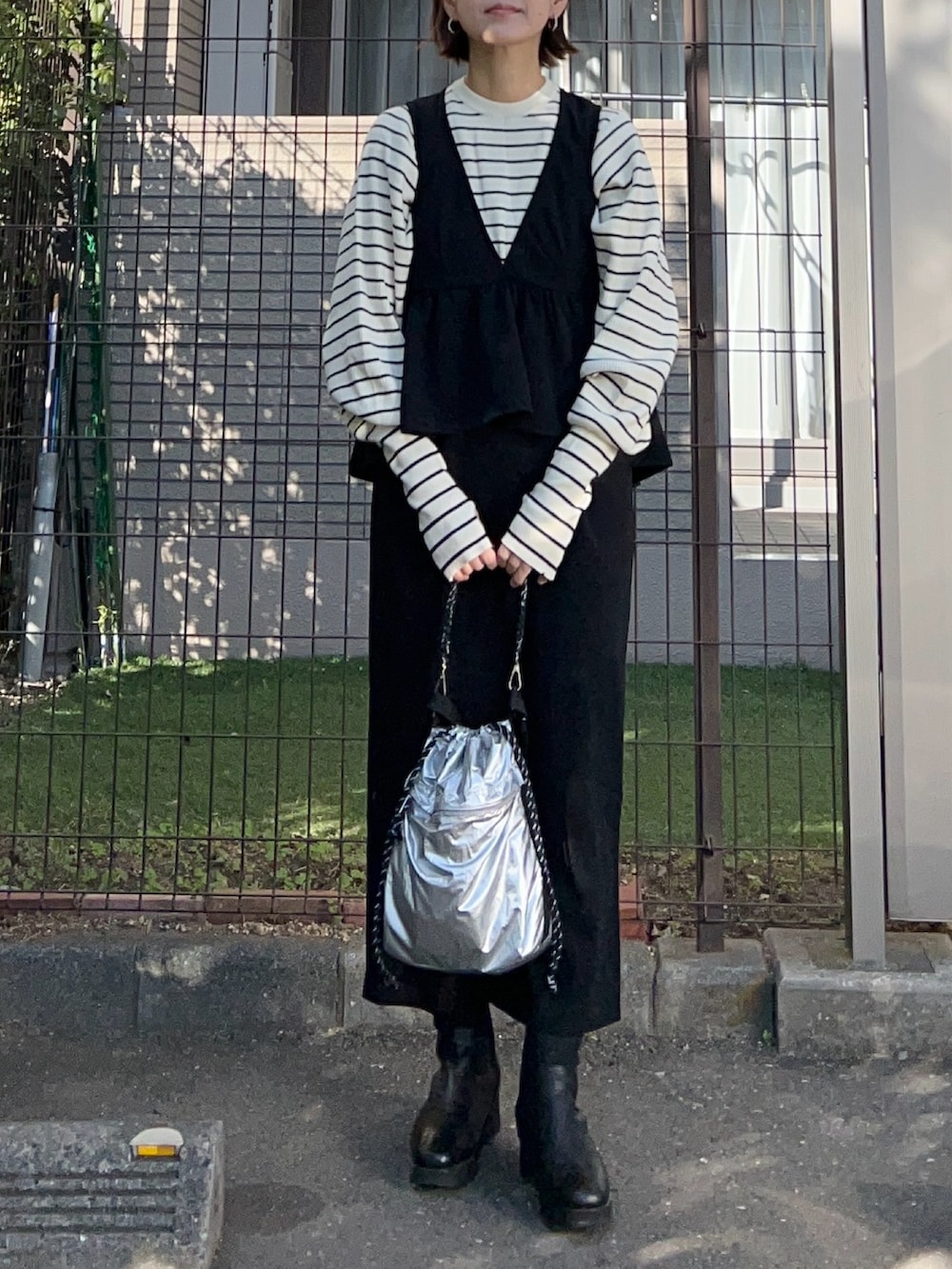 ブラック系のジャンパースカート、ホワイト系のニット/セーター、シルバー系のトートバッグを着用したレディースの冬コーディネートの2枚目の写真