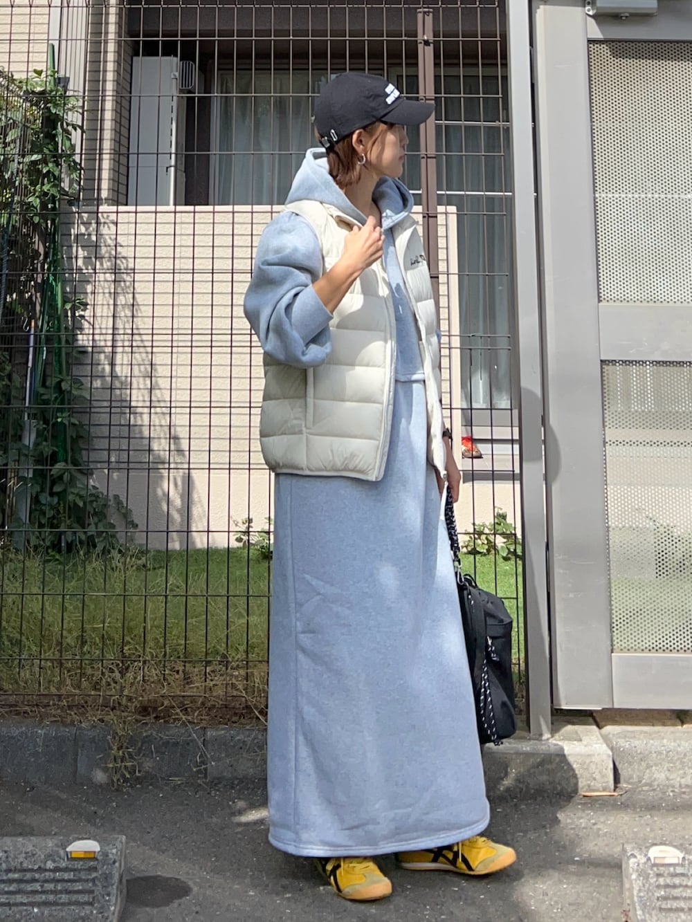 グレー系のワンピース、ブラック系のトートバッグ、ホワイト系のダウンベストを着用したレディースの秋コーディネートの2枚目の写真