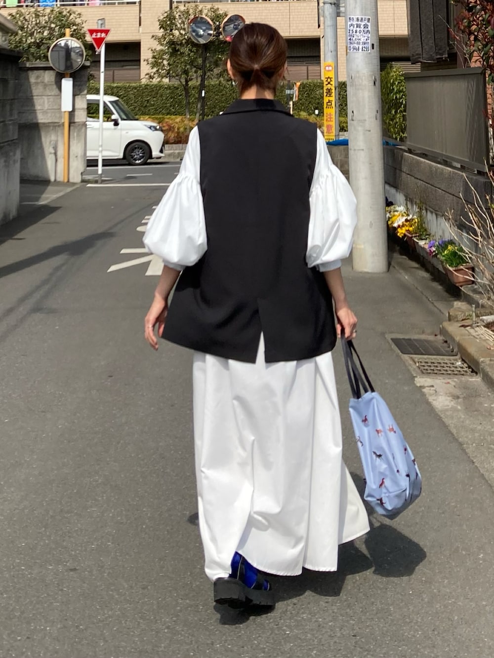 ホワイト系のワンピース、ブラック系のベスト、ブルー系のトートバッグを着用したレディースの春コーディネートの5枚目の写真