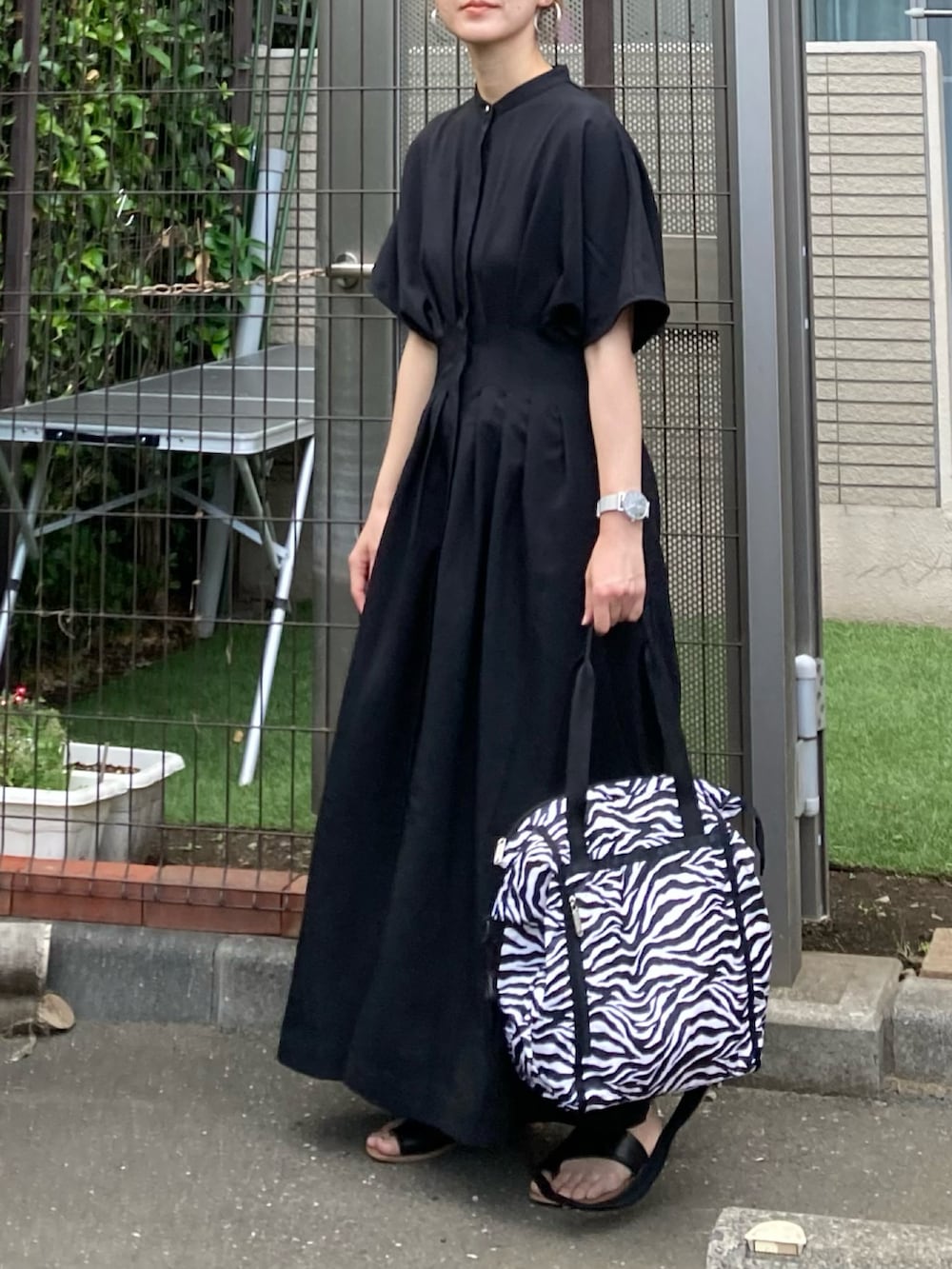 ブラック系のワンピース、ブラック系のトートバッグ、シルバー系のピアス（両耳用）を着用したレディースの夏コーディネートの2枚目の写真