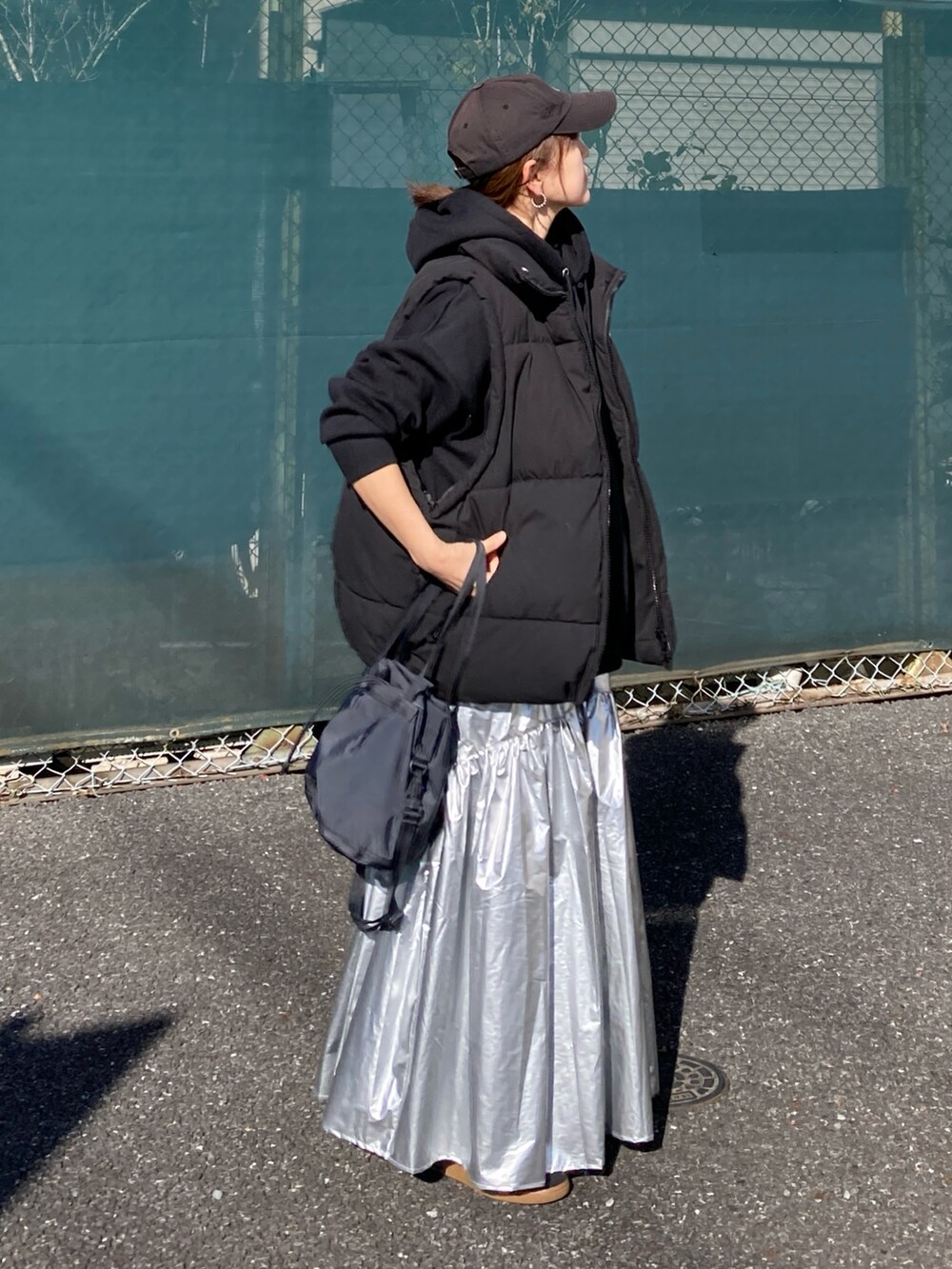 ブラック系のダウンベスト、シルバー系のスカート、ブラック系のパーカーを着用したレディースの冬コーディネートの3枚目の写真