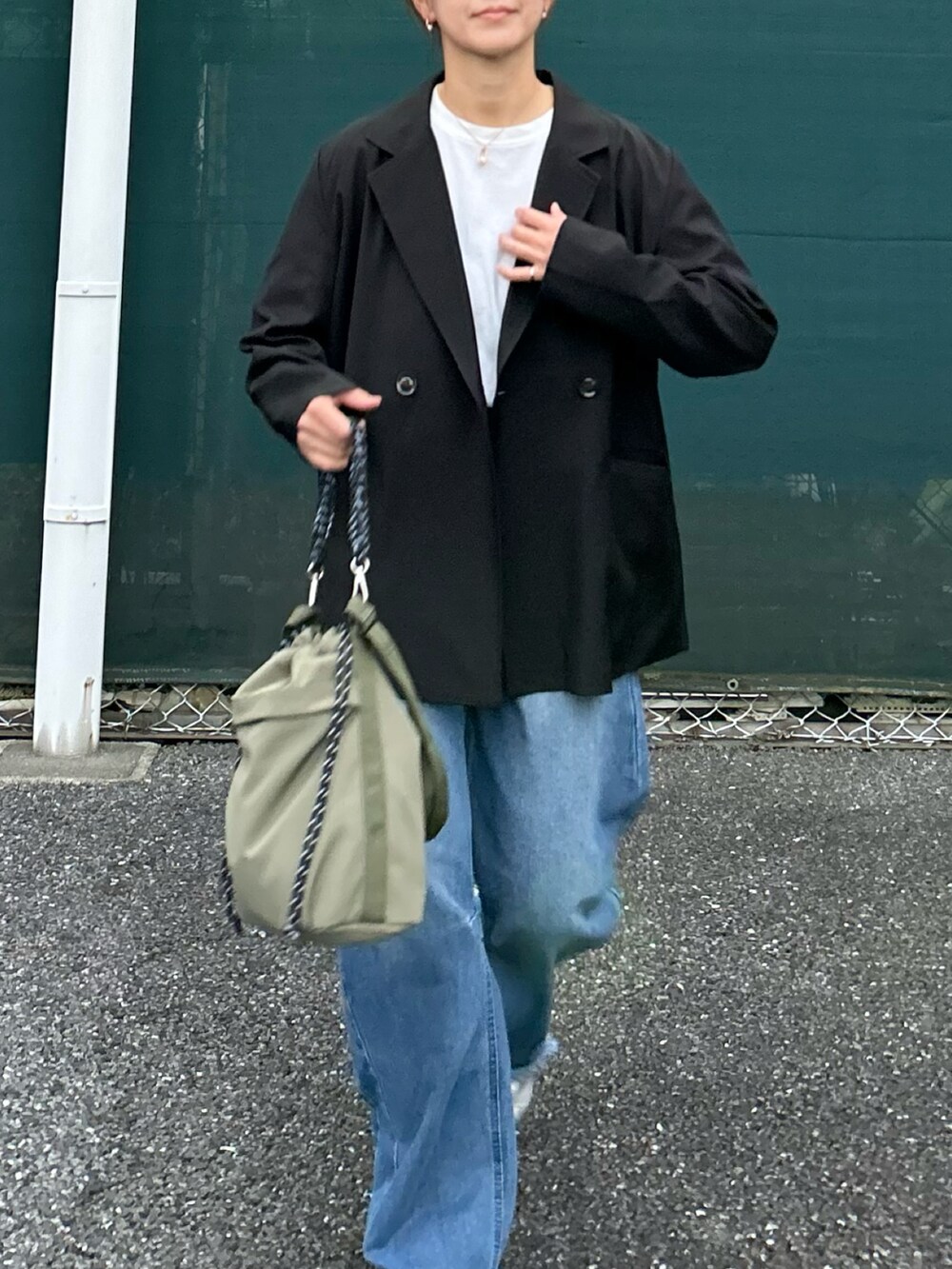 ブラック系のテーラードジャケット、ブルー系のデニムパンツ、グリーン系のトートバッグを着用したレディースの秋コーディネートの4枚目の写真