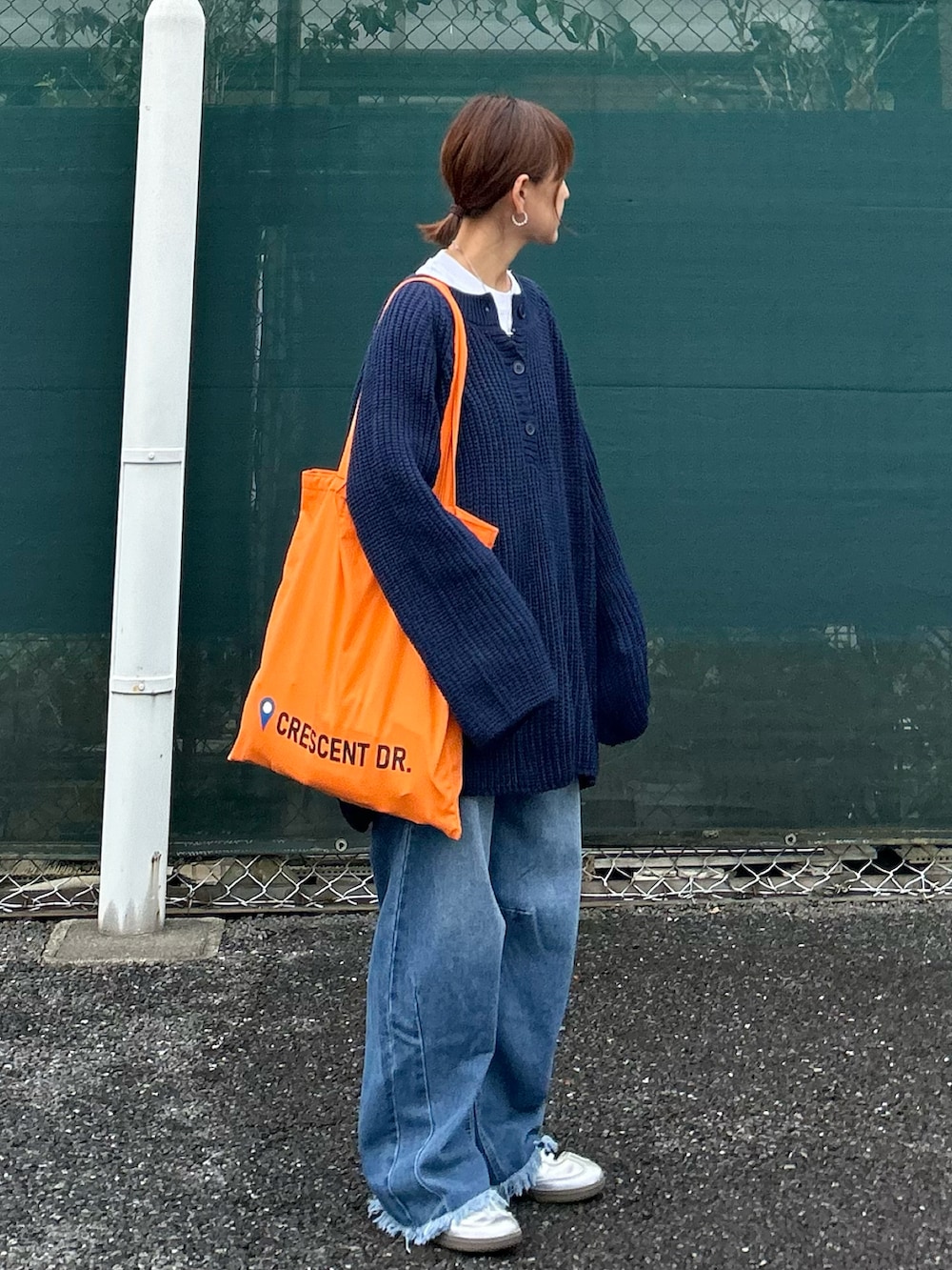 ブルー系のニット/セーター、オレンジ系のトートバッグ、ブルー系のデニムパンツを着用したレディースの秋コーディネートの3枚目の写真