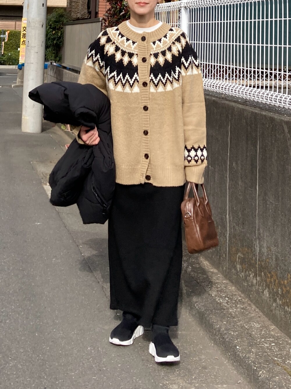 ブラック系のダウンベスト、ベージュ系のニット/セーター、ブラック系のスカートを着用したレディースの冬コーディネートの2枚目の写真