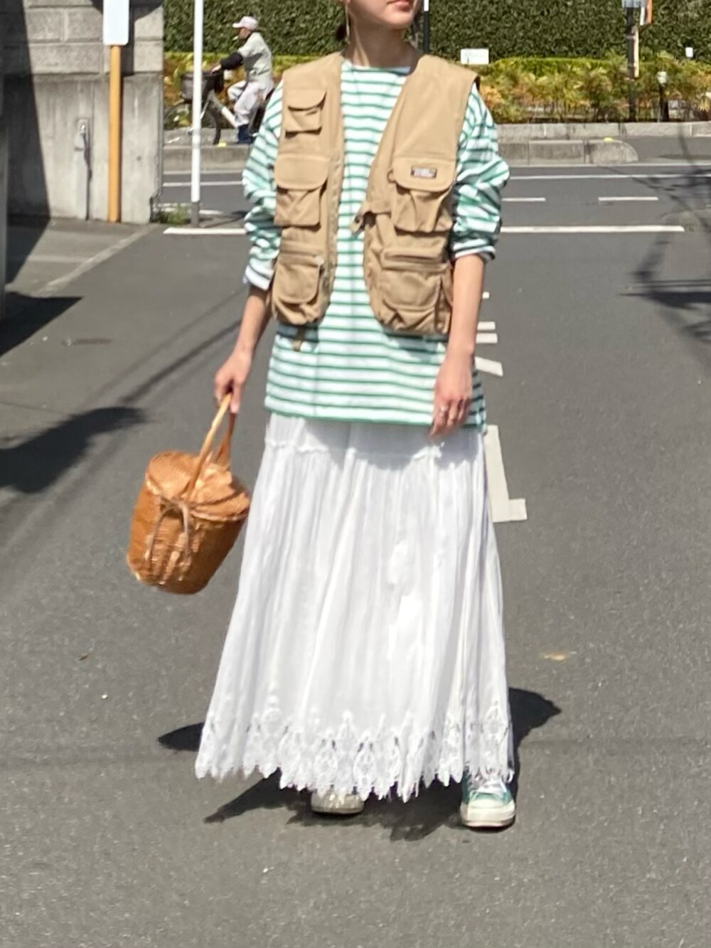 グリーン系のTシャツ/カットソー、ベージュ系のベスト、ホワイト系のスカートを着用したレディースの春コーディネートの2枚目の写真