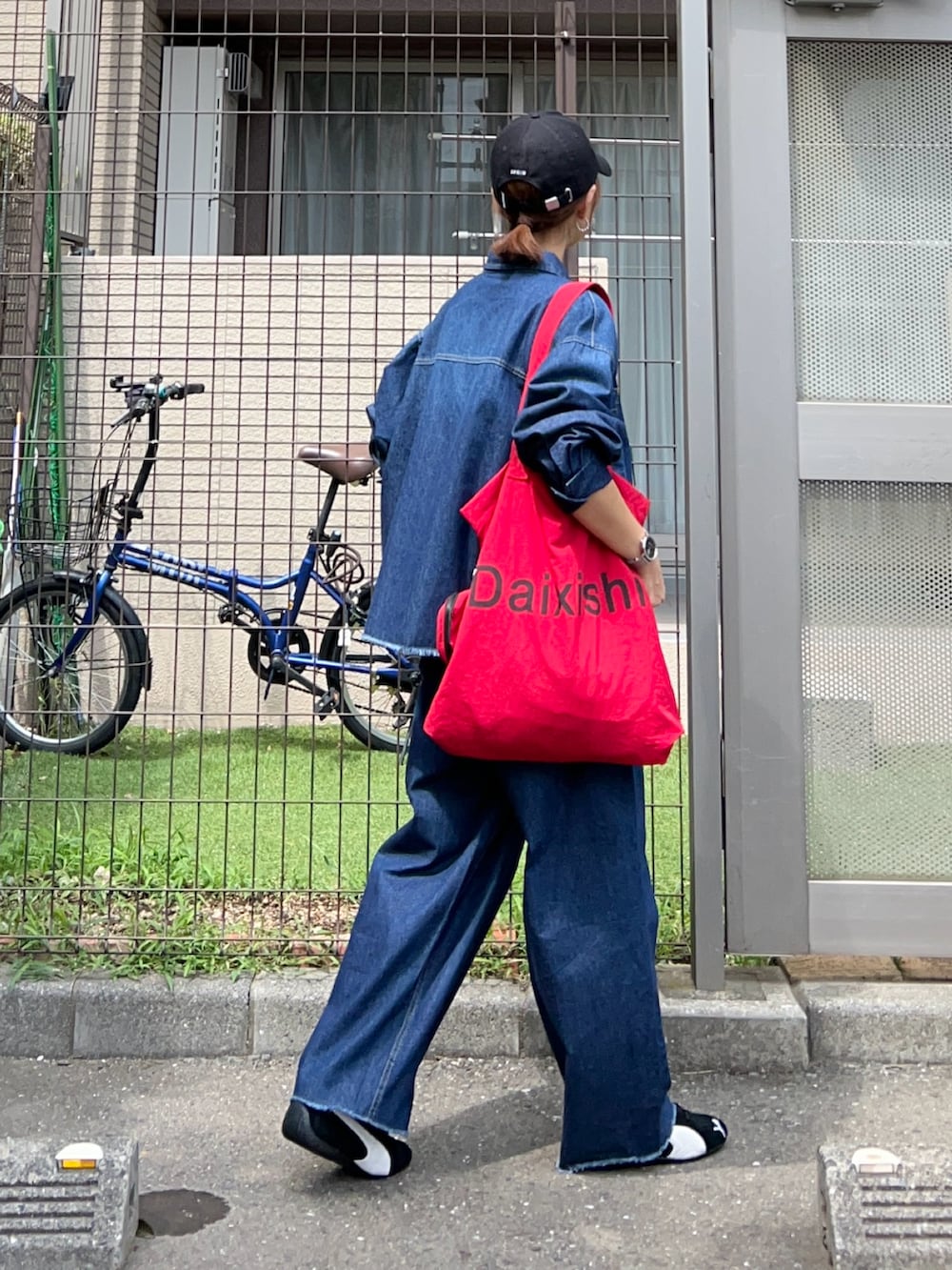 レッド系のトートバッグ、ブルー系のシャツ/ブラウス、ブルー系のデニムパンツを着用したレディースの夏コーディネートの3枚目の写真