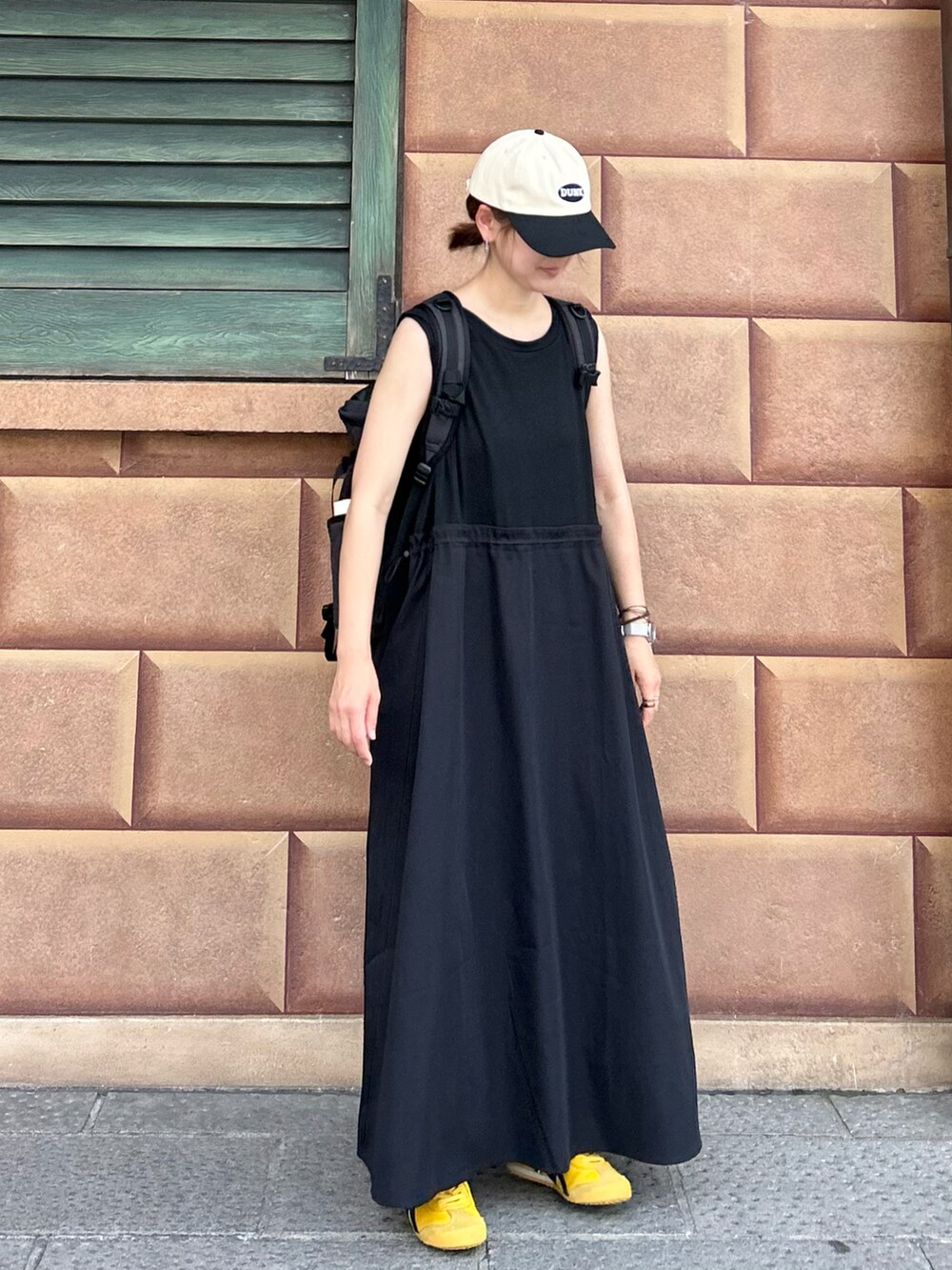 ブラック系のワンピース、イエロー系のスニーカー、ブラック系のキャップを着用したレディースの夏コーディネートの2枚目の写真