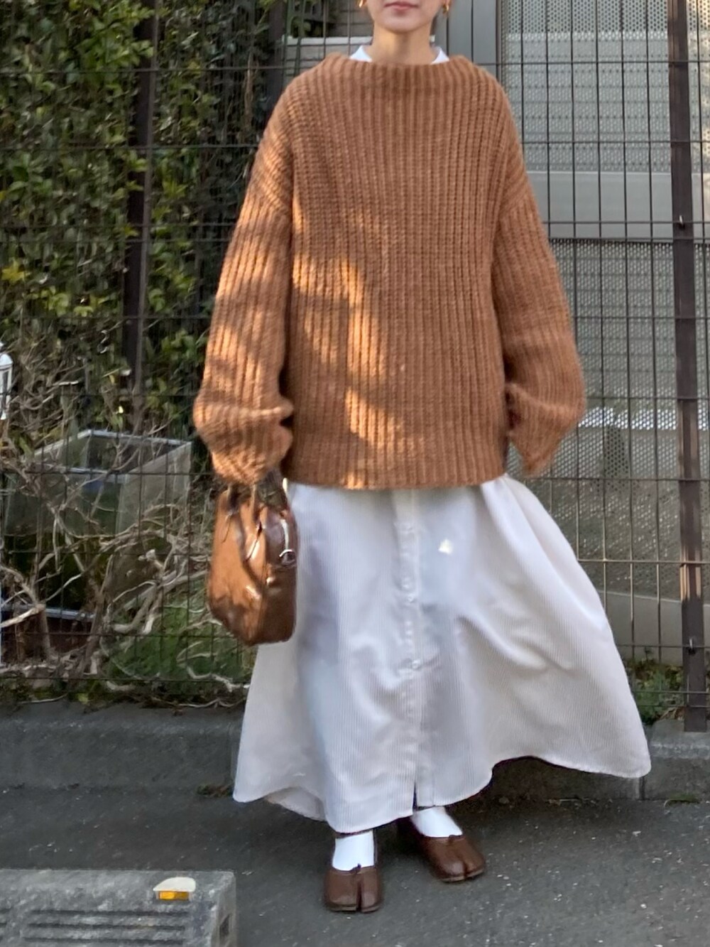 レッド系のニット/セーター、ベージュ系のワンピース、ブラウン系のショルダーバッグを着用したレディースの冬コーディネートの3枚目の写真