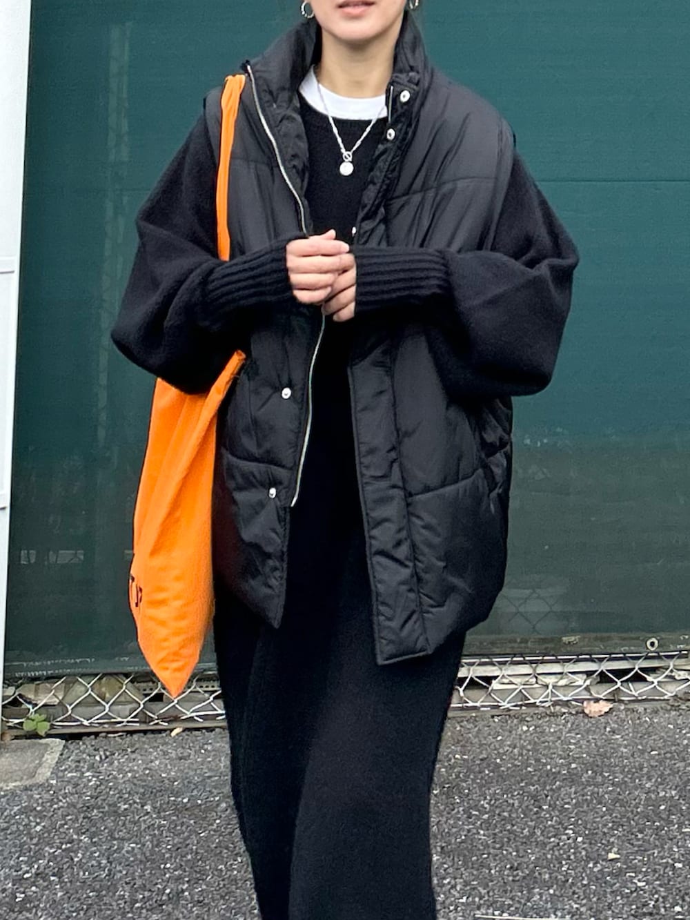 ブラック系のワンピース、ブラック系のダウンベスト、オレンジ系のトートバッグを着用したレディースの冬コーディネートの4枚目の写真