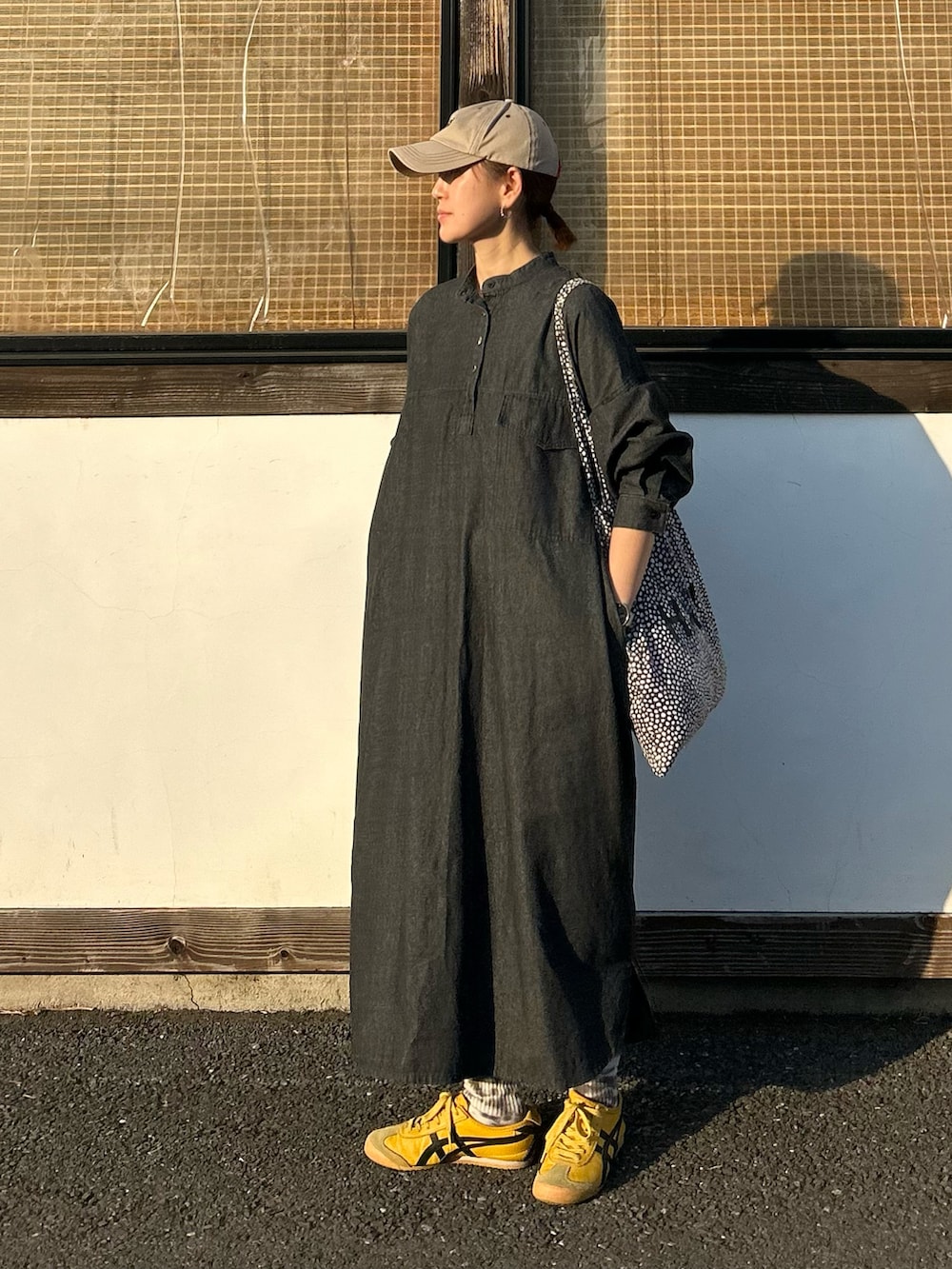 ブラック系のワンピース、イエロー系のスニーカー、ベージュ系のキャップを着用したレディースの春コーディネートの3枚目の写真