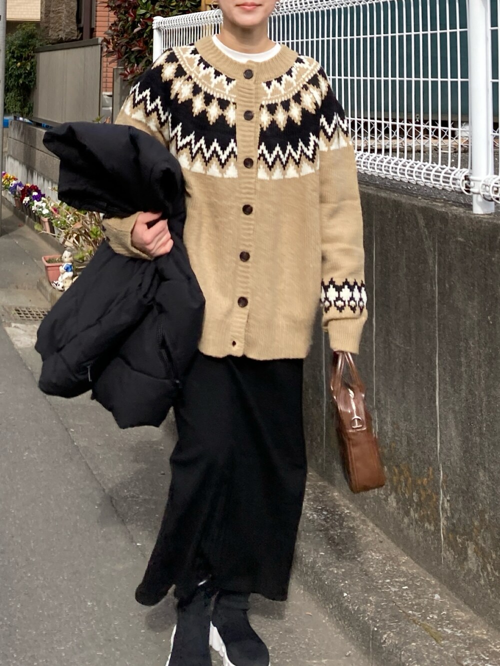 ブラック系のダウンベスト、ベージュ系のニット/セーター、ブラック系のスカートを着用したレディースの冬コーディネートの3枚目の写真