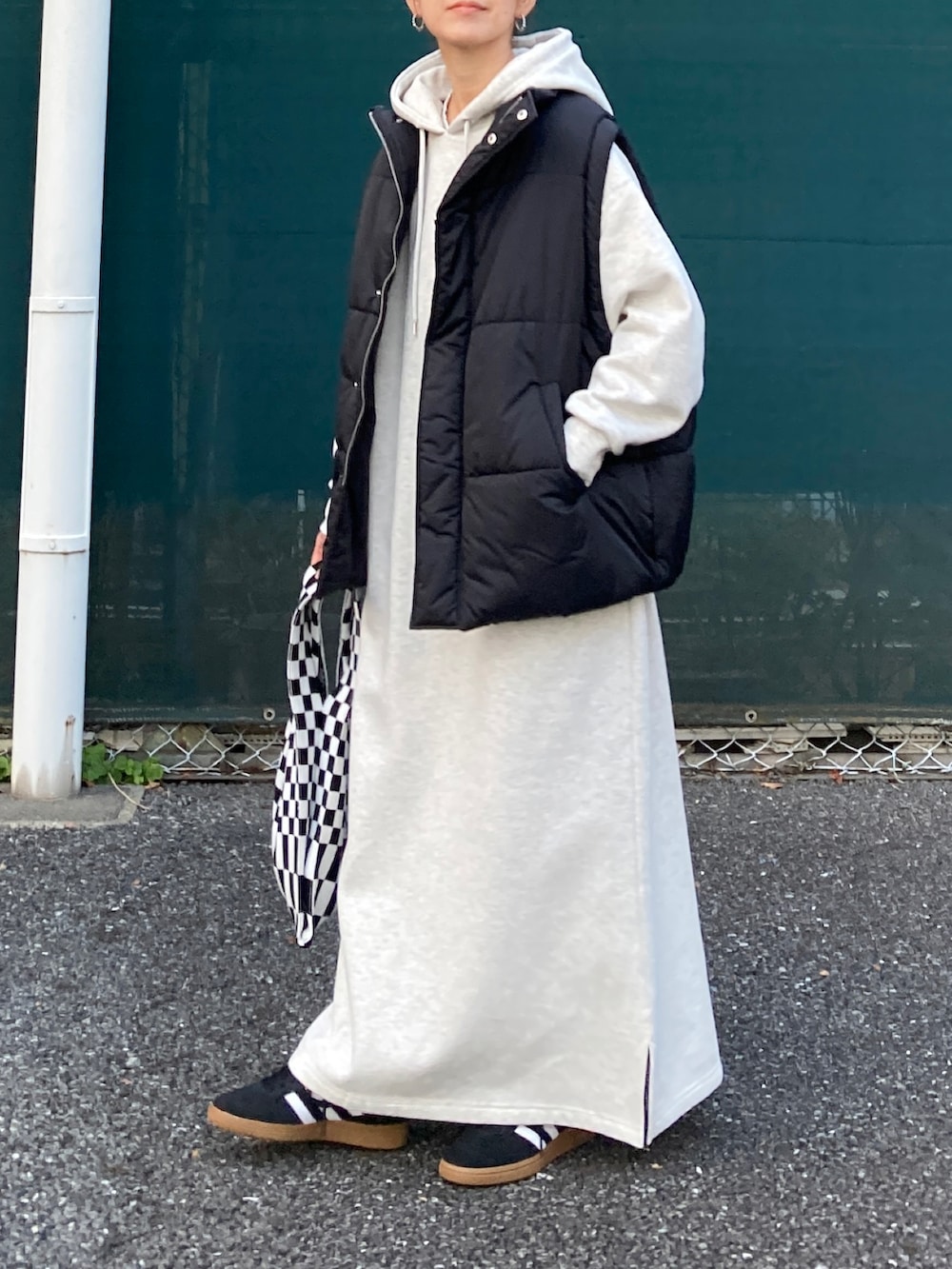 ブラック系のダウンベスト、グレー系のワンピース、ブラック系のスニーカーを着用したレディースの秋コーディネートの3枚目の写真