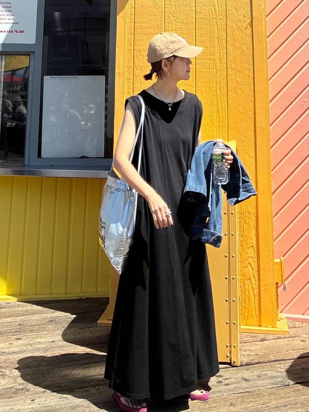 ブラック系のワンピース、シルバー系のクラッチバッグ、ベージュ系のキャップを着用したレディースの夏コーディネートの2枚目の写真