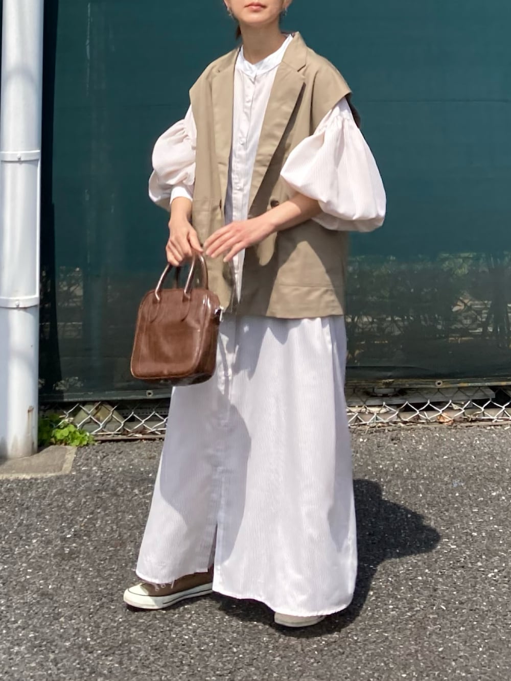 ベージュ系のベスト、ベージュ系のワンピース、ブラウン系のショルダーバッグを着用したレディースの春コーディネートの2枚目の写真