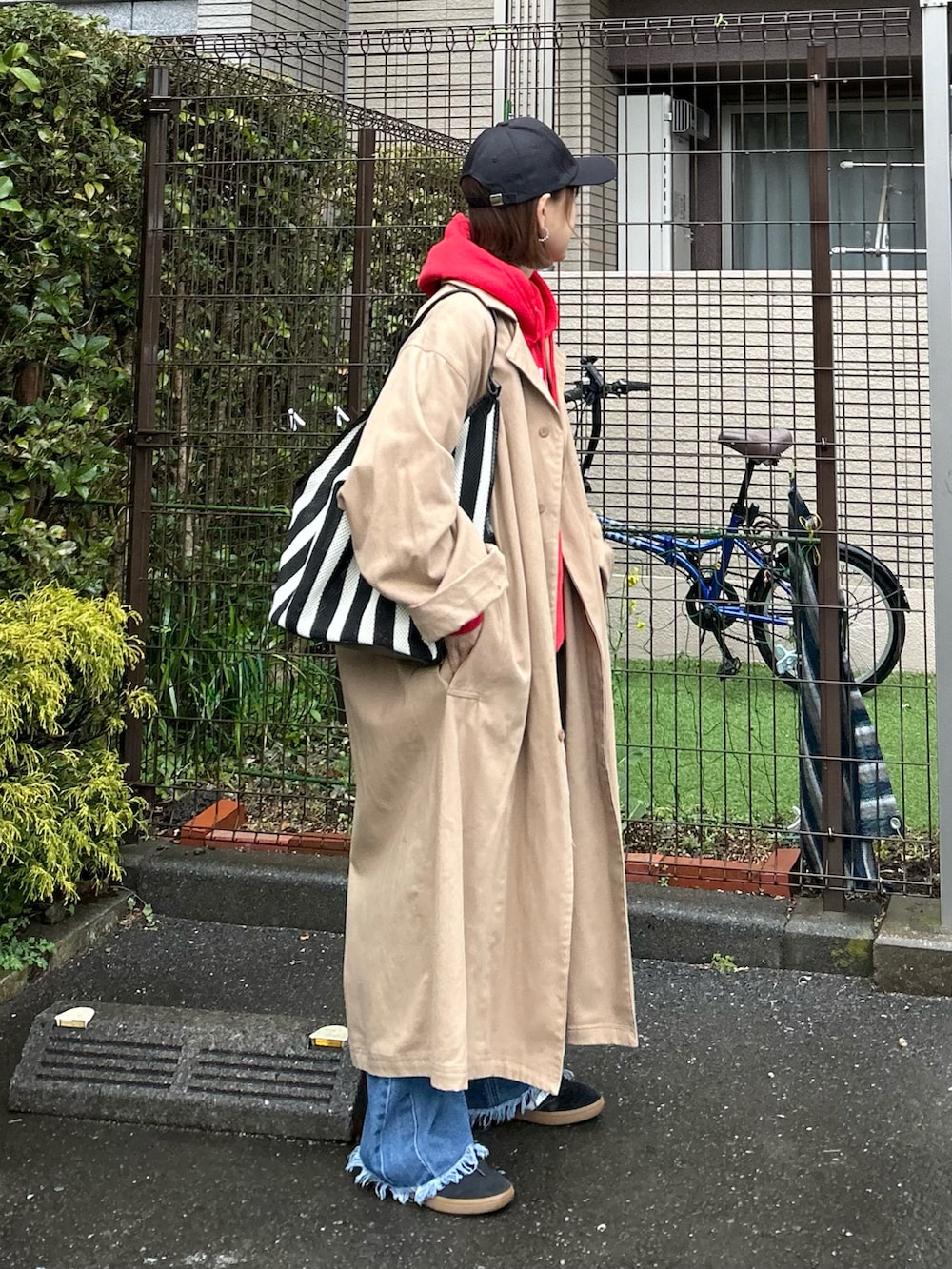 ブラック系のかごバッグ、ベージュ系のトレンチコート、ブルー系のデニムパンツを着用したレディースの春コーディネートの3枚目の写真