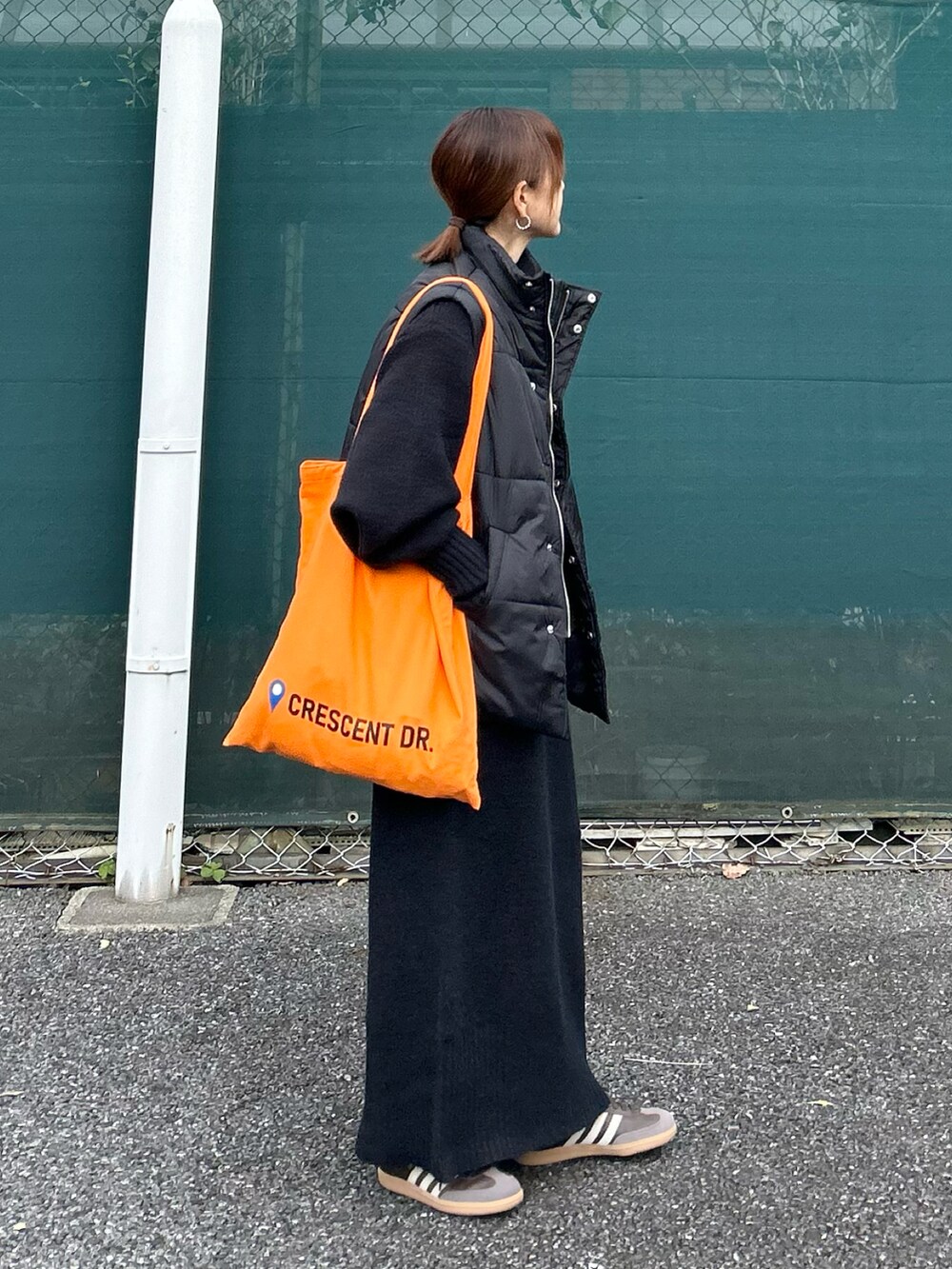 ブラック系のワンピース、ブラック系のダウンベスト、オレンジ系のトートバッグを着用したレディースの冬コーディネートの5枚目の写真