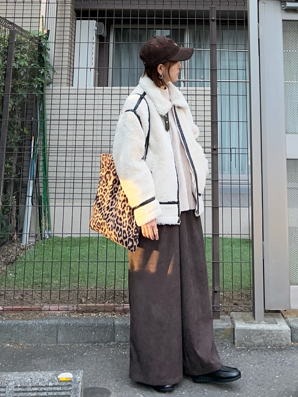 ホワイト系のムートンコート、ブラウン系のトートバッグ、ブラウン系のスラックスを着用したレディースの冬コーディネートの2枚目の写真