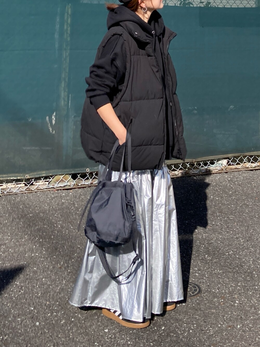 ブラック系のダウンベスト、シルバー系のスカート、ブラック系のパーカーを着用したレディースの冬コーディネートの5枚目の写真