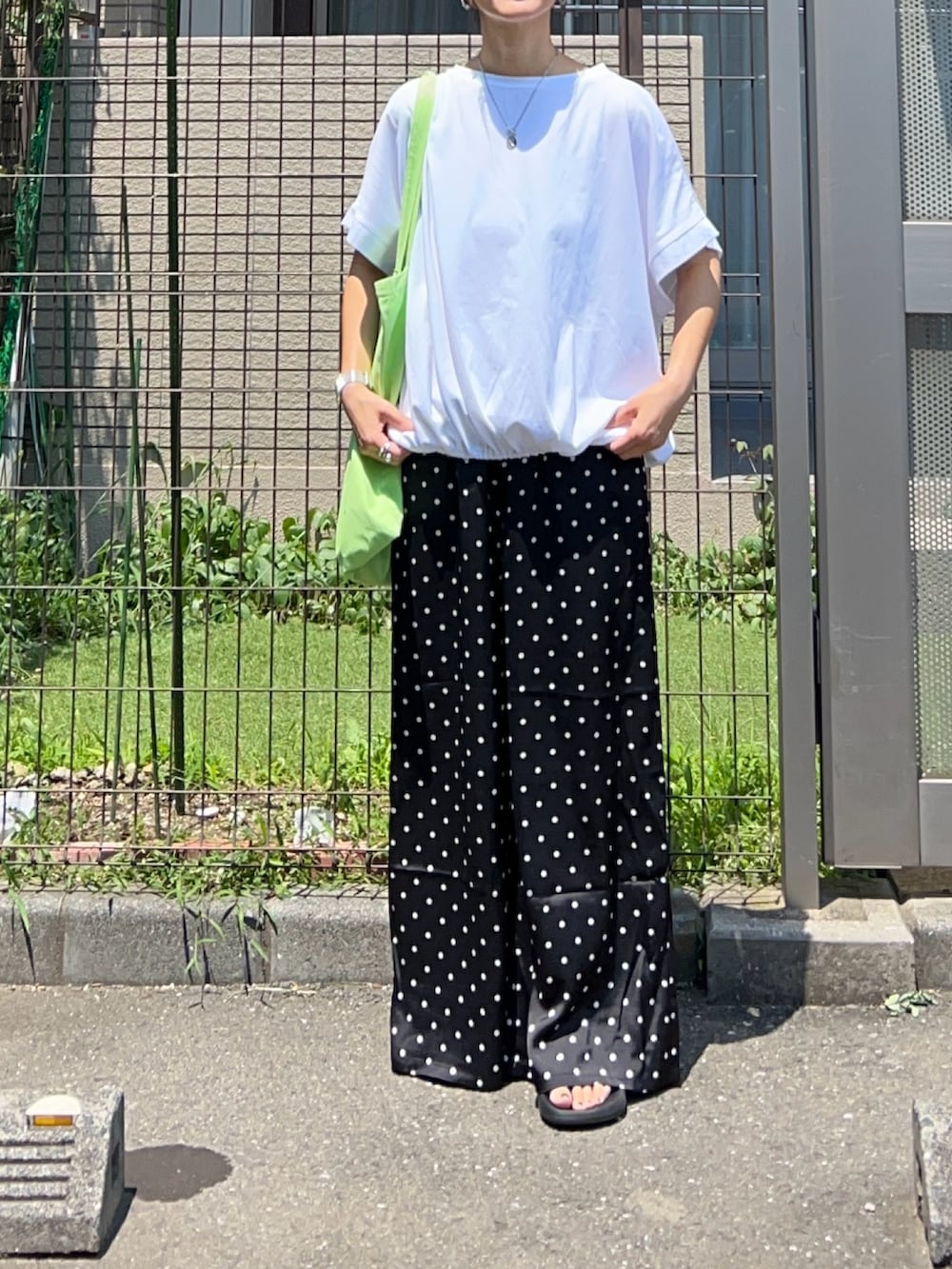 ブラック系のスラックス、グリーン系のトートバッグ、ホワイト系のTシャツ/カットソーを着用したレディースの夏コーディネートの3枚目の写真