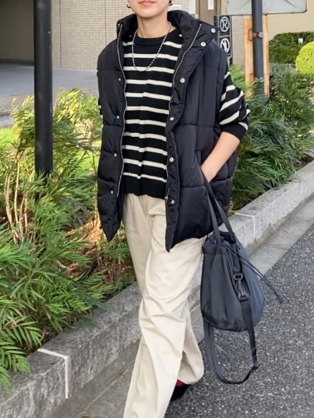 ブラック系のダウンベスト、ベージュ系のチノパンツ、ブラック系のニット/セーターを着用したレディースの秋コーディネートの3枚目の写真