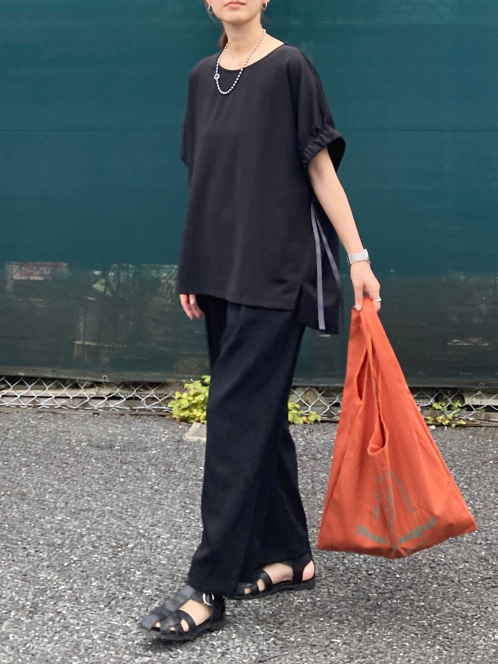 ブラック系のTシャツ/カットソー、ブラック系のその他パンツ、オレンジ系のトートバッグを着用したレディースの夏コーディネートの2枚目の写真