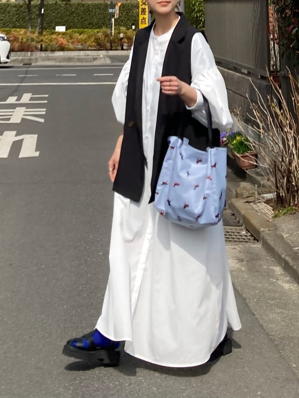 ホワイト系のワンピース、ブラック系のベスト、ブルー系のトートバッグを着用したレディースの春コーディネートの4枚目の写真