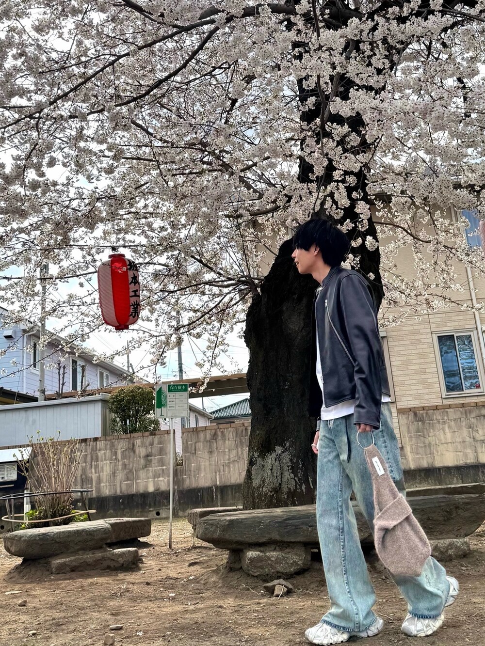 グレー系のスニーカー、ブラック系のライダースジャケット、ブルー系のデニムパンツを着用したメンズの春コーディネートの2枚目の写真