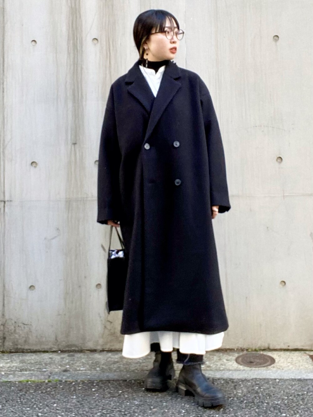 ブラック系のチェスターコート、ホワイト系のワンピース、ブラック系のTシャツ/カットソーを着用したレディースの秋コーディネートの2枚目の写真