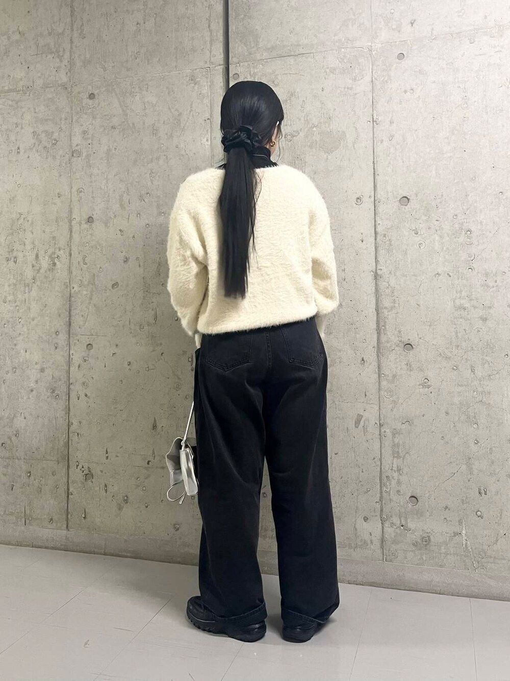 ブラック系のデニムパンツ、シルバー系のショルダーバッグ、ホワイト系のニット/セーターを着用したレディースの冬コーディネートの3枚目の写真