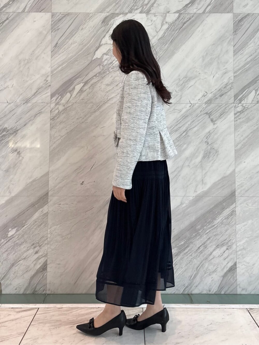 ブルー系のノーカラージャケット、ブルー系のスカート、ブラック系のハンドバッグを着用したレディースの春コーディネートの3枚目の写真