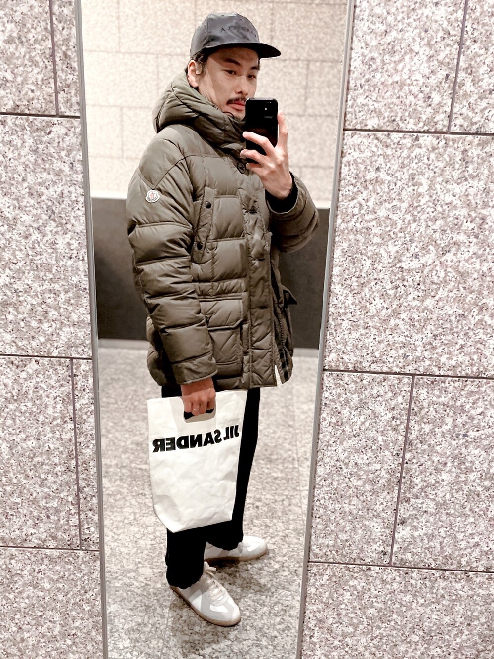 グリーン系のダウンジャケット/コート、ブラック系のその他パンツ、ホワイト系のハンドバッグを着用したメンズの冬コーディネートの2枚目の写真