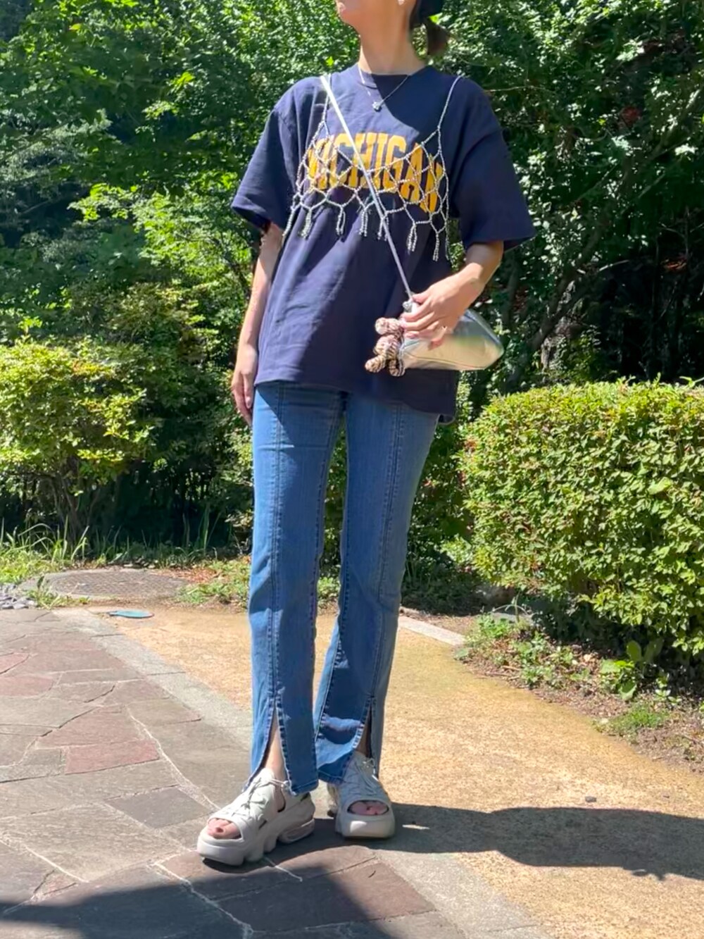 シルバー系のベスト、シルバー系のショルダーバッグ、ブルー系のデニムパンツを着用したレディースの夏コーディネートの3枚目の写真