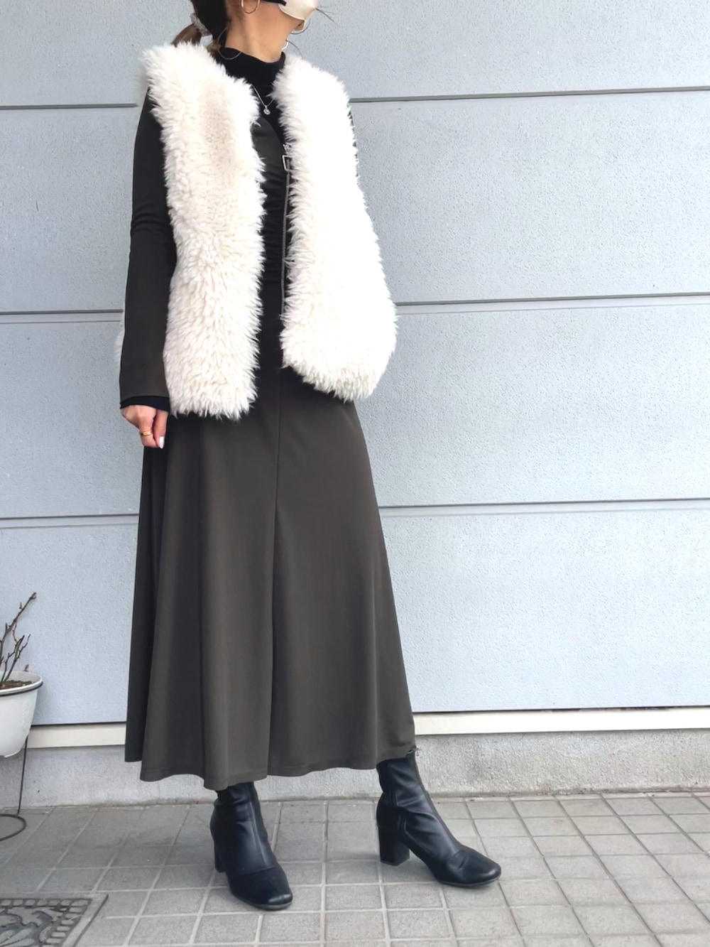 グリーン系のワンピース、ホワイト系のベスト、ブラック系のブーティを着用したレディースの冬コーディネートの2枚目の写真