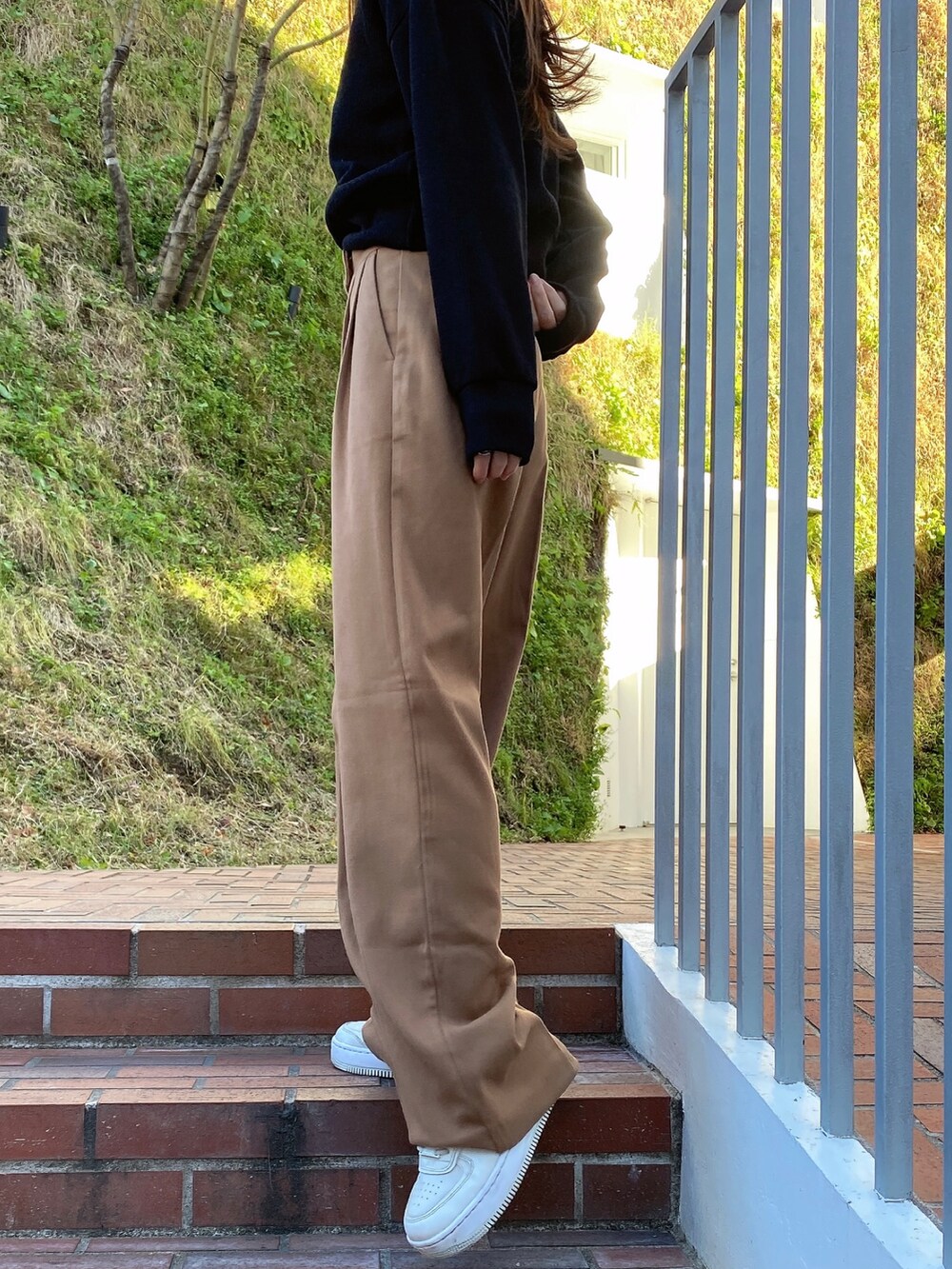 ブラック系のトップス、ブラウン系のスラックス、ホワイト系のスニーカーを着用したレディースの冬コーディネートの2枚目の写真