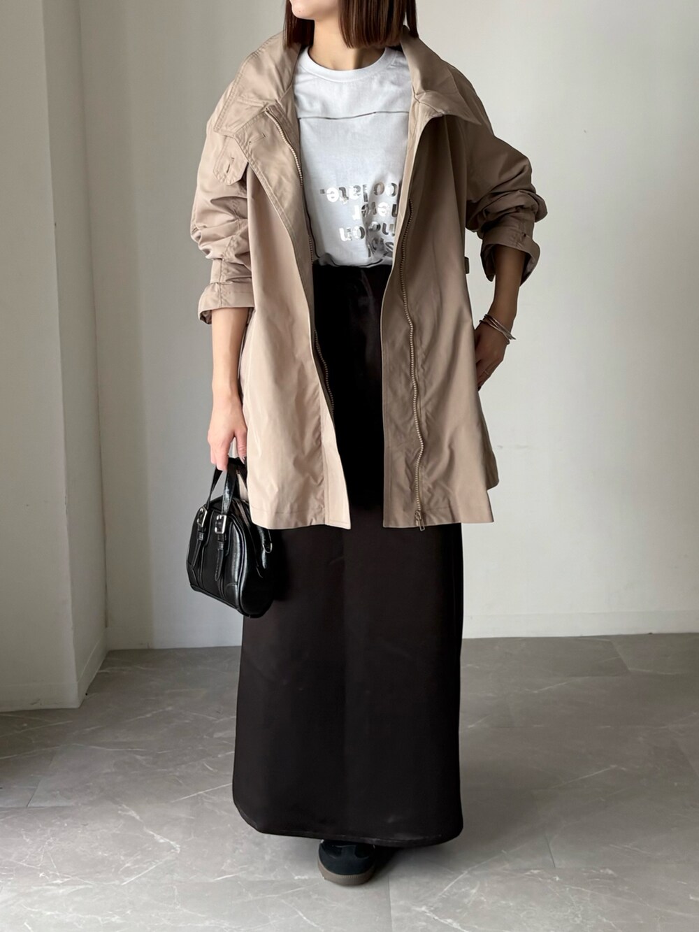 ベージュ系のトレンチコート、ブラック系のスカート、その他のTシャツ/カットソーを着用したレディースの春コーディネートの2枚目の写真