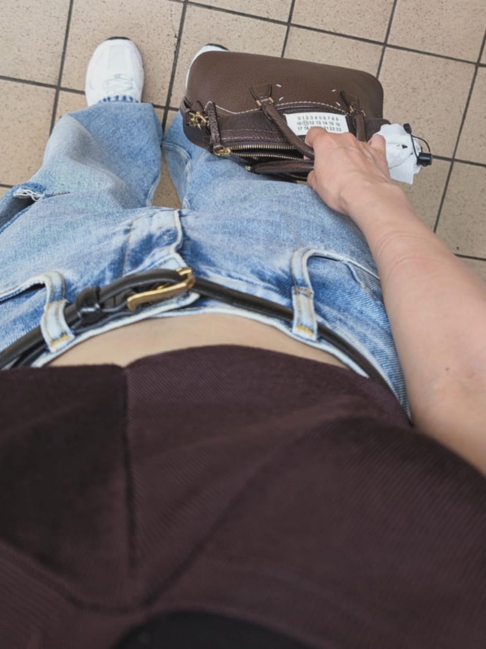 ブラウン系のバッグ、ブルー系のデニムパンツ、ホワイト系のスニーカーを着用したレディースの夏コーディネートの2枚目の写真