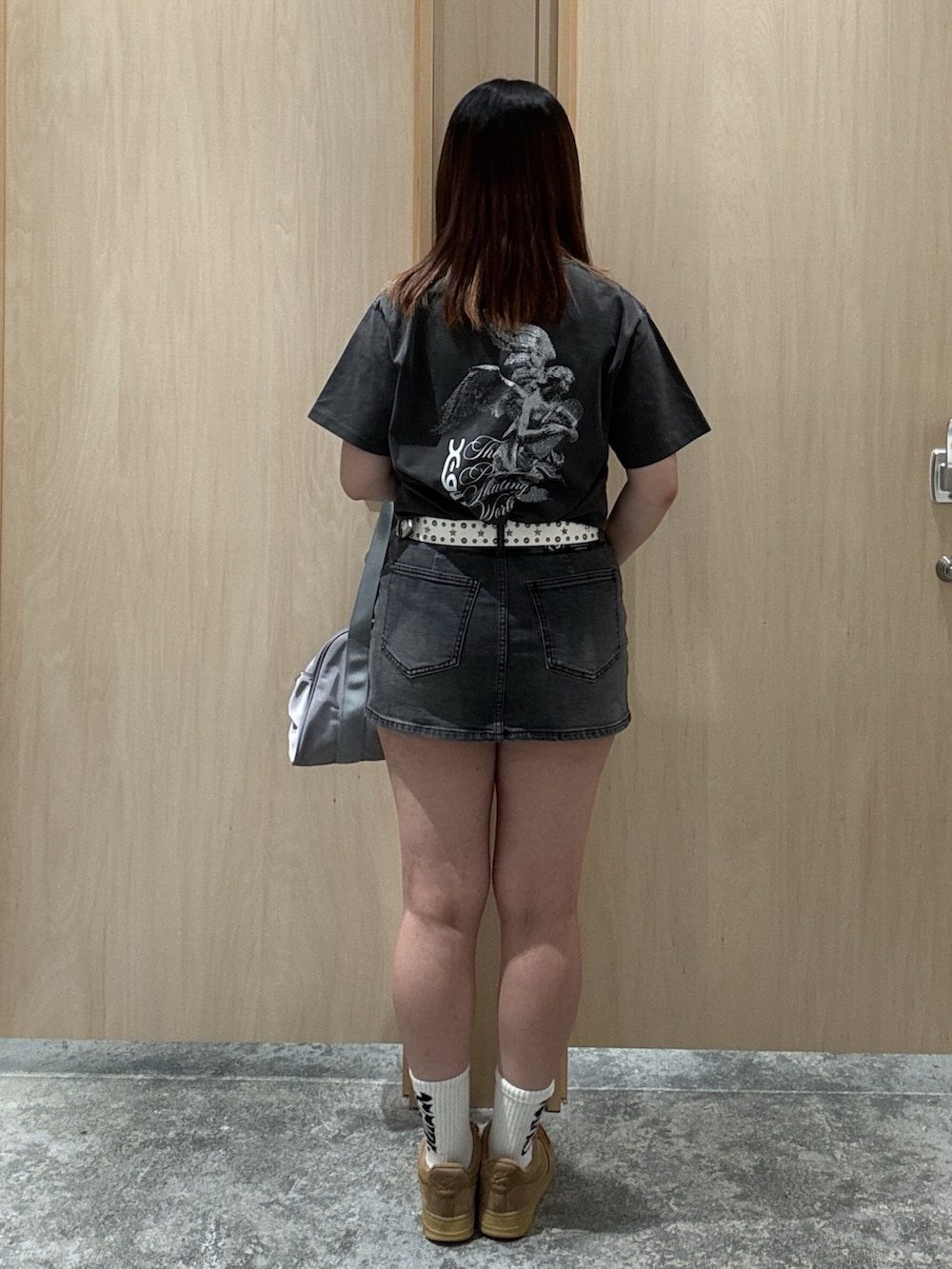 ブラック系のデニムスカート、ブラック系のTシャツ/カットソー、グレー系のハンドバッグを着用したレディースの夏コーディネートの2枚目の写真