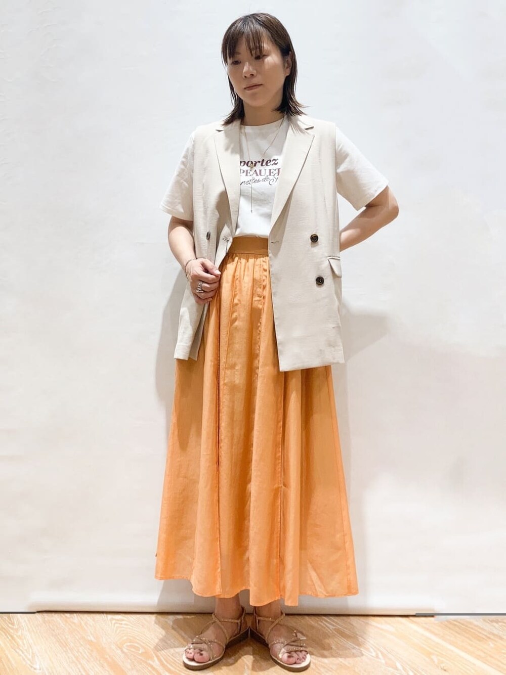 ホワイト系のTシャツ/カットソー、ベージュ系のベスト、オレンジ系のスカートを着用したレディースの春コーディネートの2枚目の写真