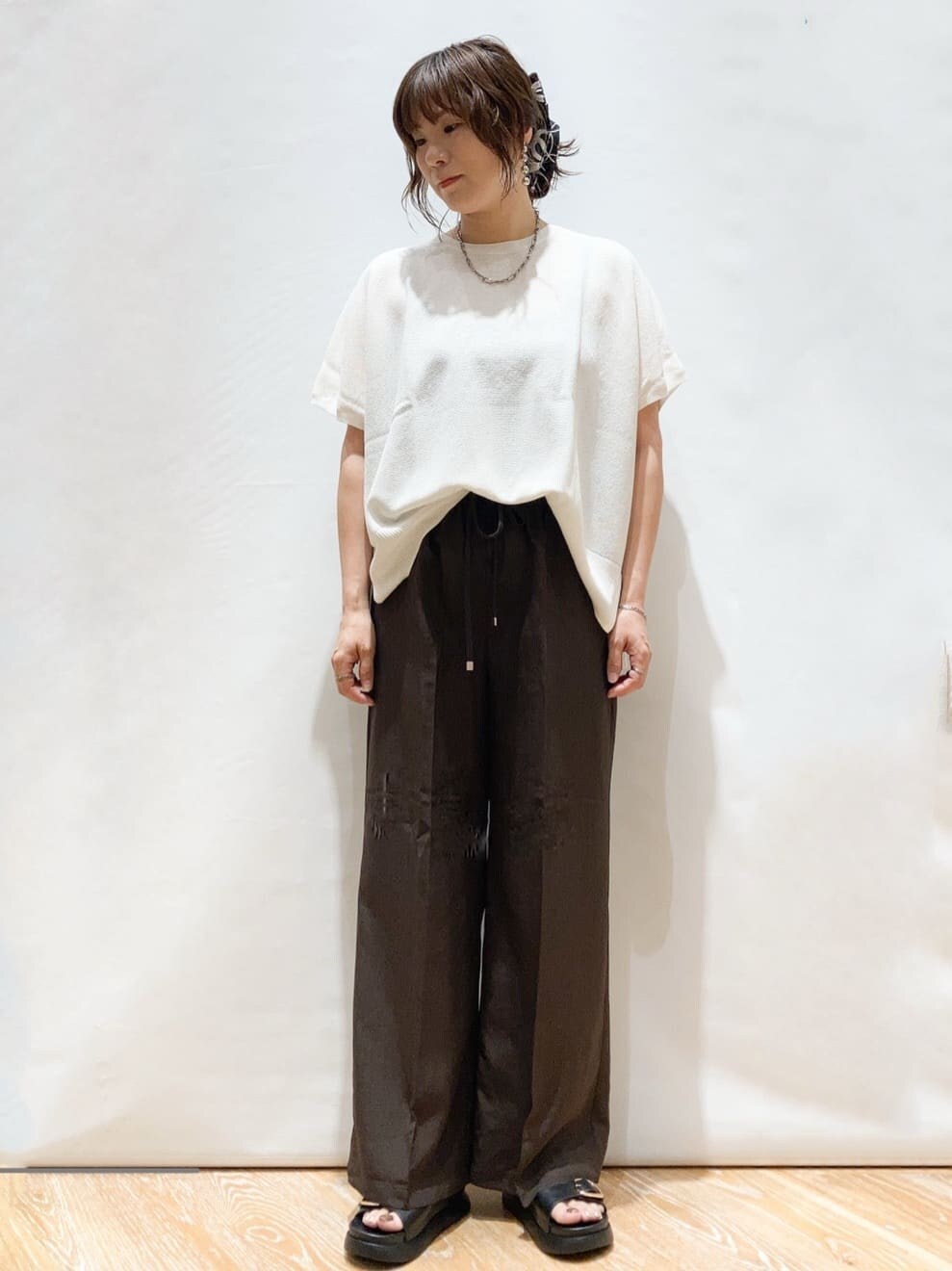 ホワイト系のニット/セーター、ブラウン系のその他パンツ、ブラック系のトートバッグを着用したレディースの夏コーディネートの2枚目の写真